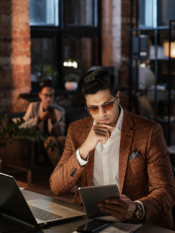 Man in brown blazer reviewing tablet at office desk