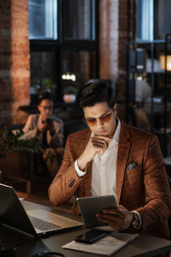 Man in brown blazer reviewing tablet at office desk